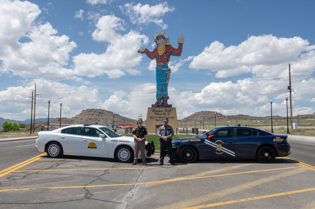 UHP Trooper and Nevada State Trooper stand by their vehicles with Wendover Will sign in the background.