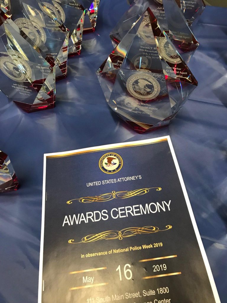 Cover of program for US Attorney's Awards Ceremony with awards in the background.