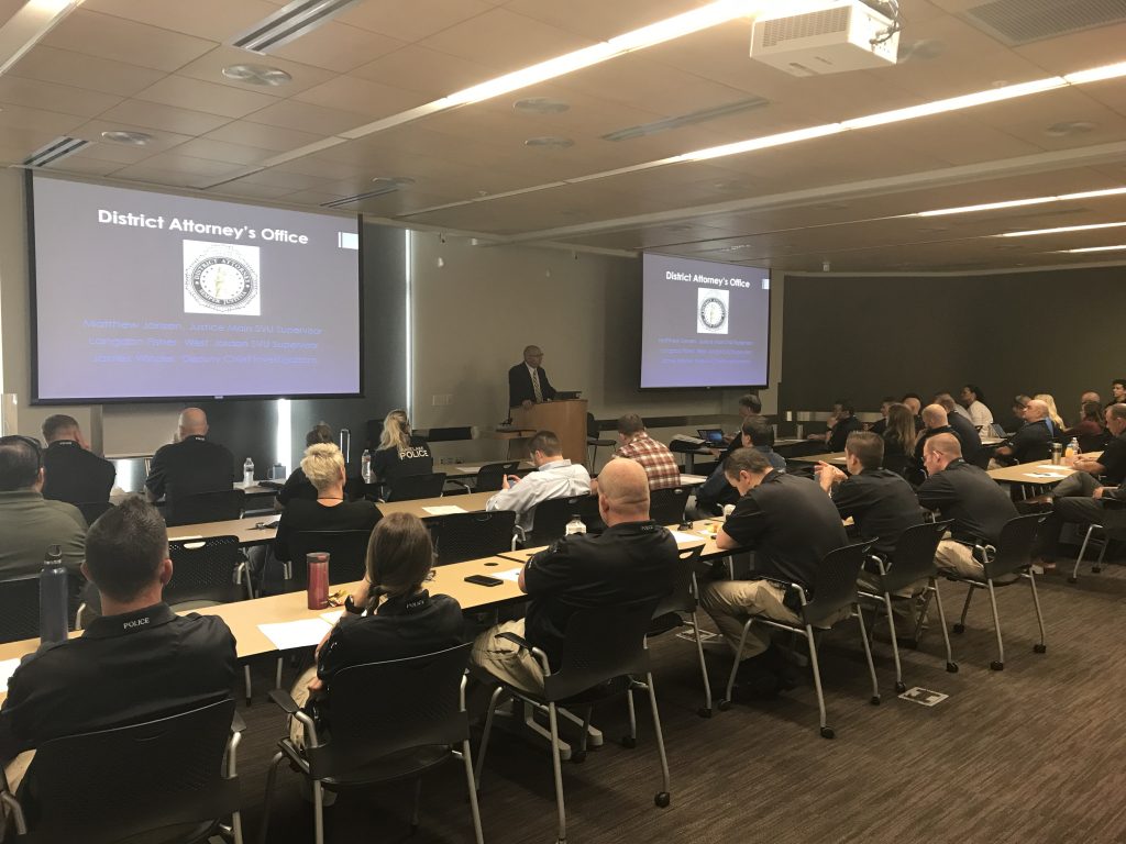 Sex crimes investigators attend a class at which they received a legislative update. Photo shows flyer announcing training and officers listening as Matt Janzen from the Salt Lake County DA's Office provides them with information.