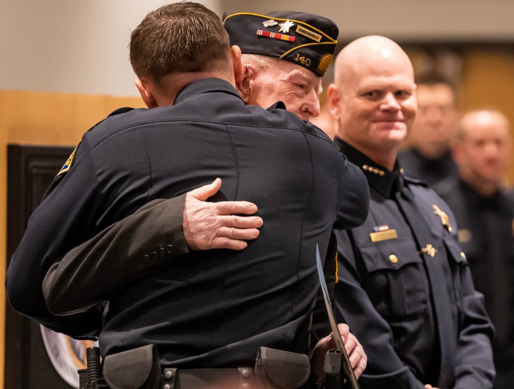 A new officer hugs his relative who is presenting him with his law enforcement certificate.